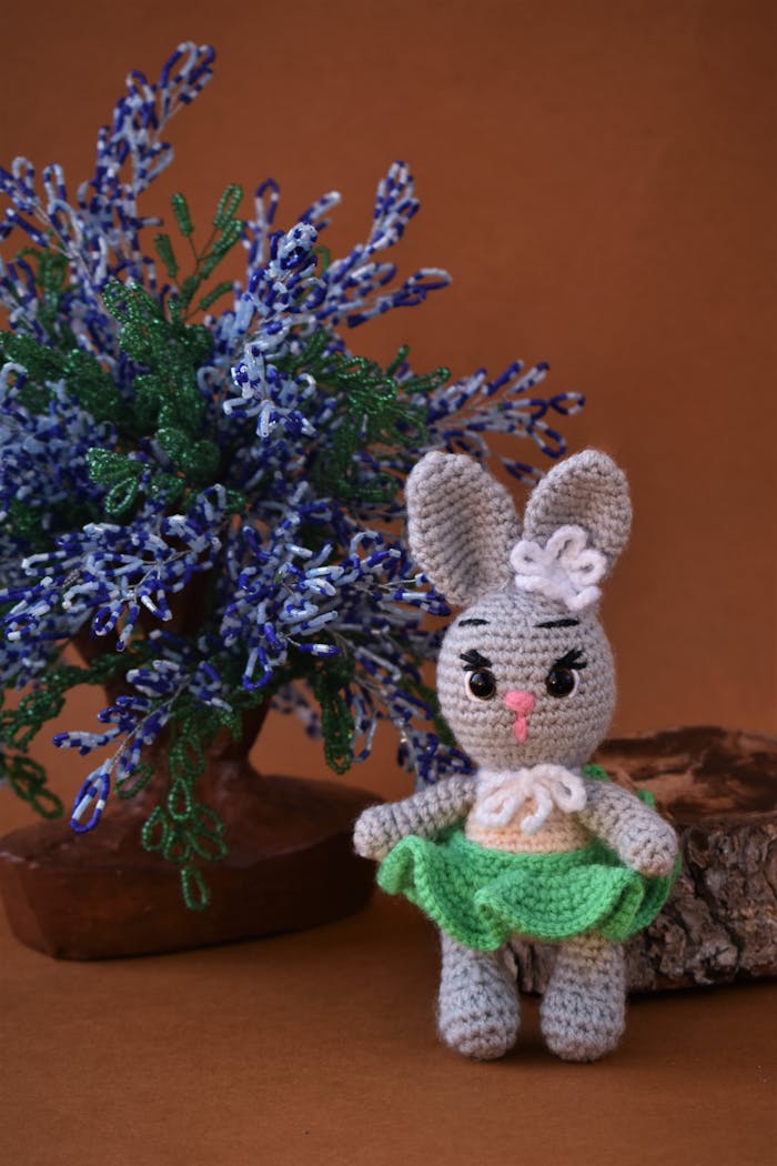 Cute crochet bunny doll with a colorful tree backdrop on brown background.